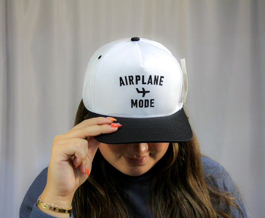 Person wearing a white and black cap with 'AIRPLANE MODE' text against a plain background